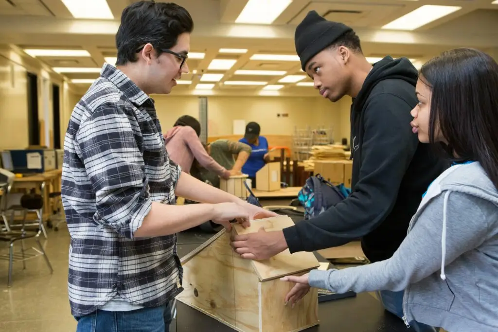 An engineering teacher helps two twelfth-grade students secure the roof on the blue jay house they built.