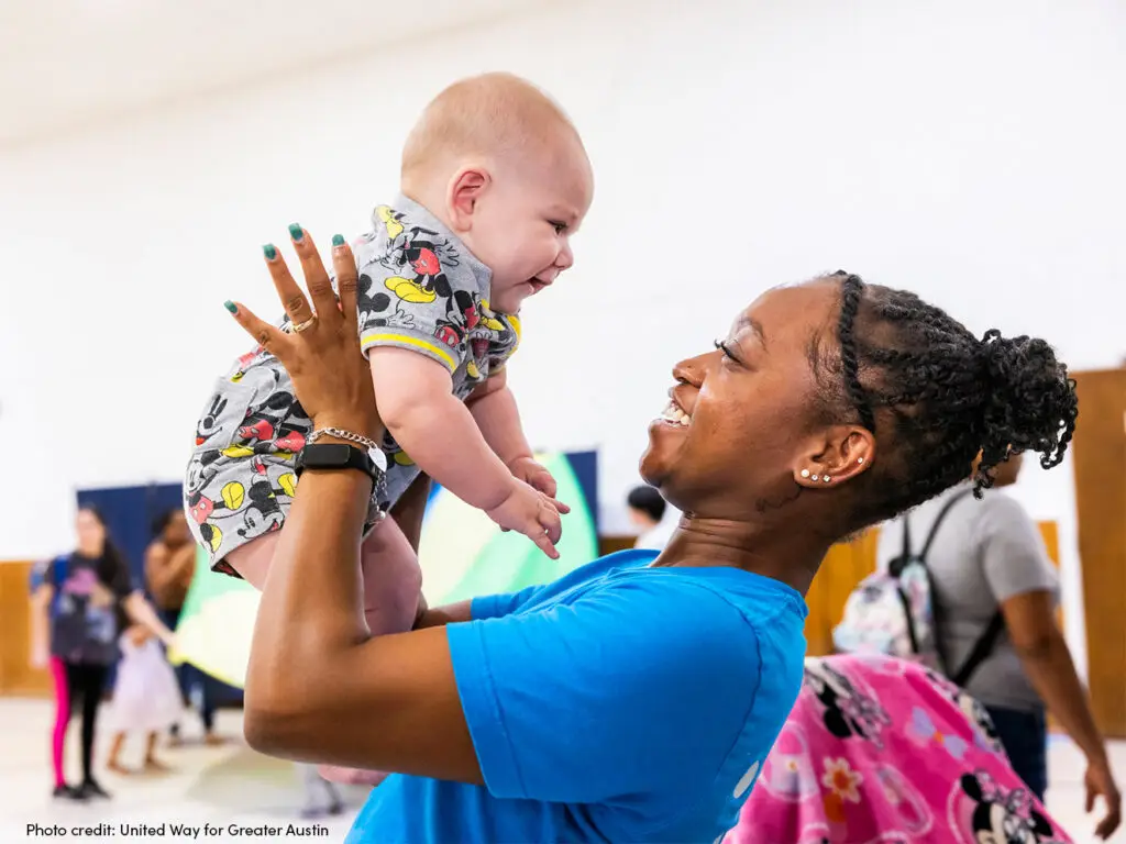 Woman holding up a baby and they are looking at each other smiling.