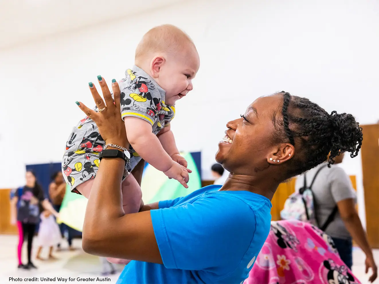 Woman holding up a baby and they are looking at each other smiling.