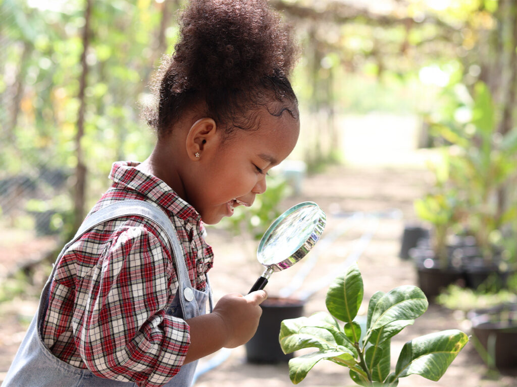 Young child inspecting plant with magnifying glass