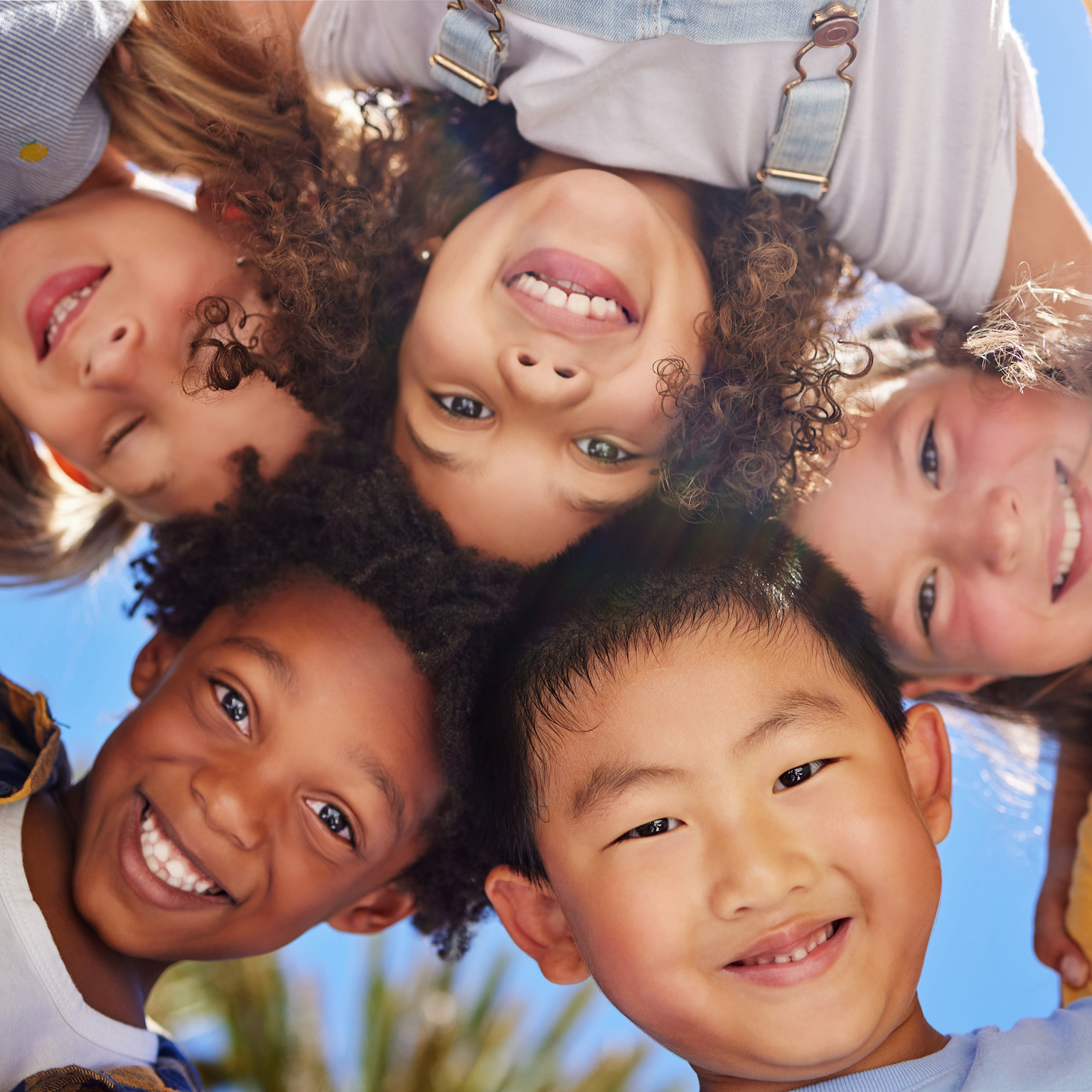 Diverse group of kids with heads together looking downward into camera