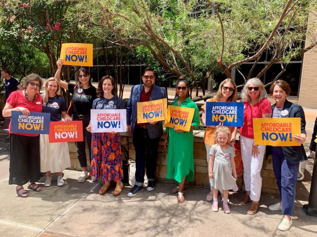 Group from the community holding up signs together that say Affordable Childcare Now.