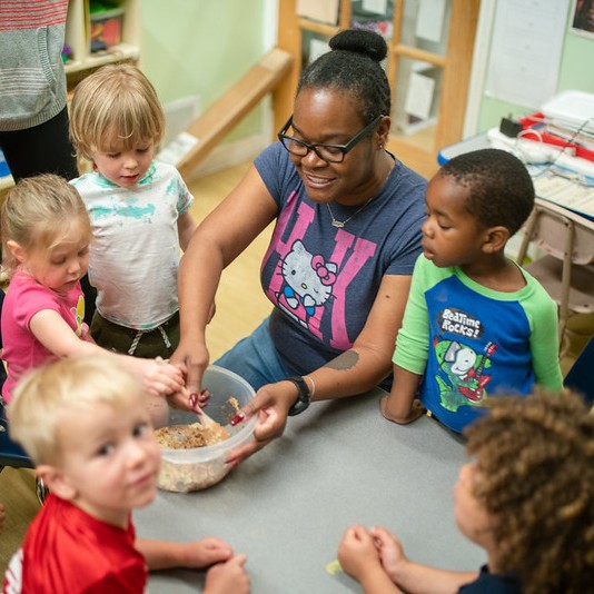 An adult teaching cooking to a group of young children.