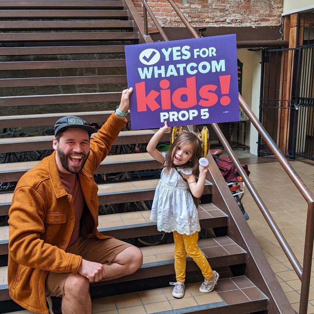 Adult helping child hold up campaign sign.